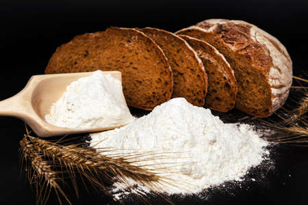 Bread, flour, spikelets of wheat on a black background. Flour is the main ingredient for baking.の写真素材