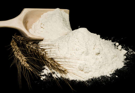 Flour. Scoop with flour and wheat ears close up on black background