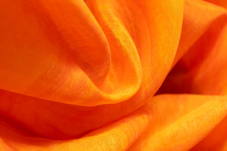 Background from material of yellow-orange color. Fabric with pleats and waves. Light orange tint patternの写真素材