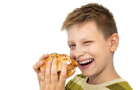 Boy eating burger on a white background. Teenager in braces. Harmful food for childrenの写真素材