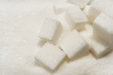 Refined sugar cubes are scattered over loose sugar. Sucrose ingredient for confectionery