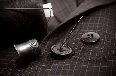 A needle and thread sews up a button on a plaid suit. Thimble. Textileの写真素材