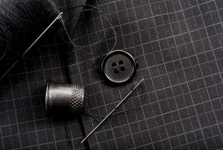 A needle and thread sews up a button on a plaid suit. Thimble. Textileの写真素材