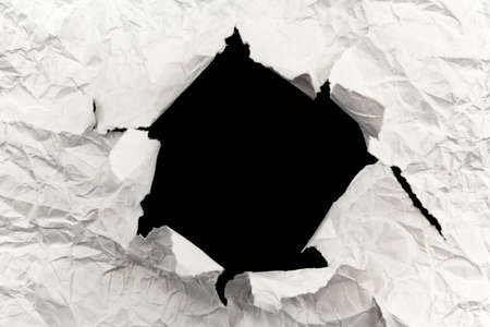 A hole in white paper with torn edges and a black isolated background inside, Ripped black and white paper, copy spaceの写真素材