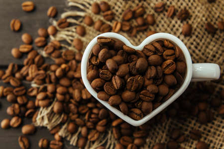 Coffee beans. Coffee beans pouring out of heart shaped cup on fabric and wooden backgroundの写真素材