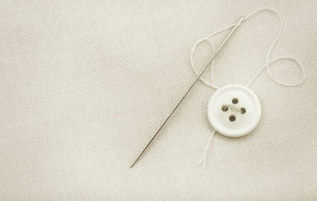 The needle and thread lie on a white cloth. Button on clothing. Seamstress and tailor tools