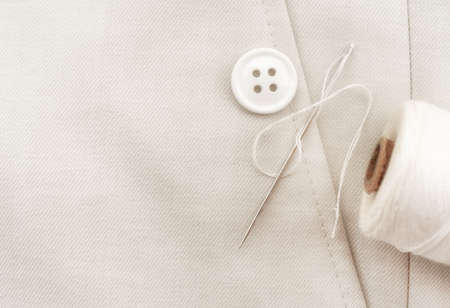 Needle with white threads, buttons on white fabric, clothes. Part of men's clothing.の写真素材
