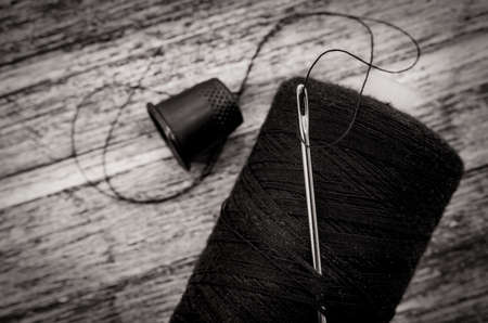 Needle with black thread. Spool of thread close up on wooden backgroundの写真素材