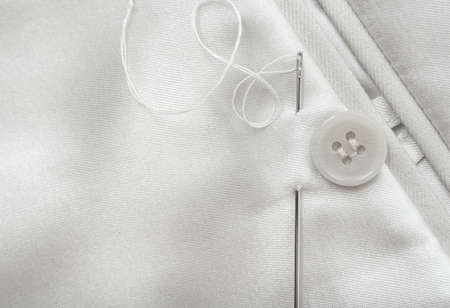 The needle and thread lie on a white cloth. Button on clothing. Seamstress and tailor tools