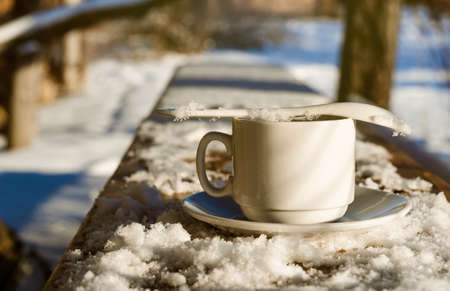 Cup of coffee in the shape of a heart on a snowy wooden table. Coffee on a sunny winter morningの写真素材