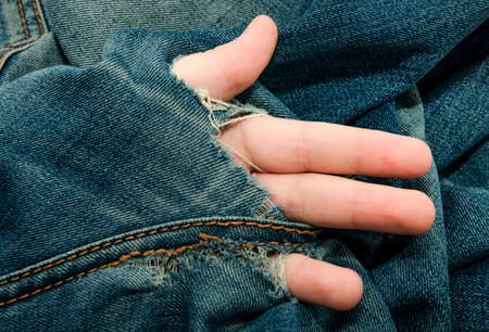 Hole in jeans. Hand with fingers climbs out of a hole in jeansの写真素材