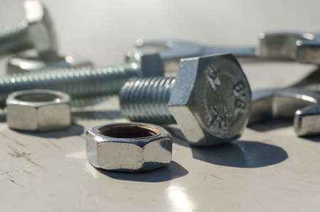 Bolts and nuts are scattered on a wooden surface close-up. Construction
