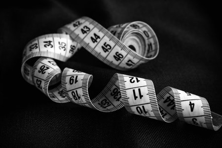 A centimeter is a tool for a tailor, fashion designer or seamstress. The centimeter lies on a piece of black clothの写真素材