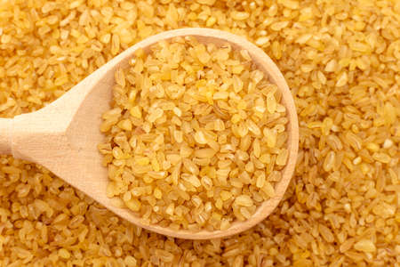 Bulgur wheat background. Bulgur grains lie in a wooden spoon. View from aboveの写真素材