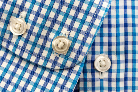 Buttons on the sleeve of the shirt in blue checkered material. button