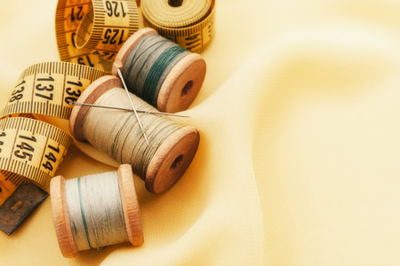 Old retro sewing accessories lie on a yellow fabric. Needle and thread