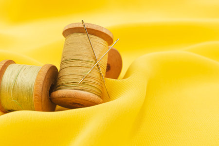 Old retro sewing accessories lie on a yellow fabric. Needle and threadの写真素材