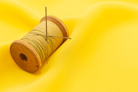 Old retro sewing accessories lie on a yellow fabric. Needle and threadの写真素材