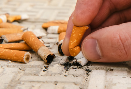 The man's hand extinguishes a lit cigarette. Cigarettes are harmful to health