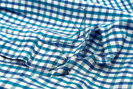 A needle and thread lies on torn or holey clothes. Shirt with a hole. Work for a seamstress or...