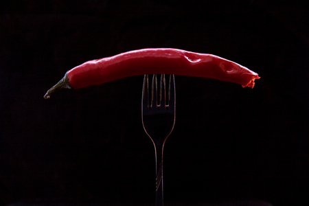 Kiev, Ukraine - February 26, 2018: Snacked hot pepper, pinned on a fork on a black background.のeditorial素材