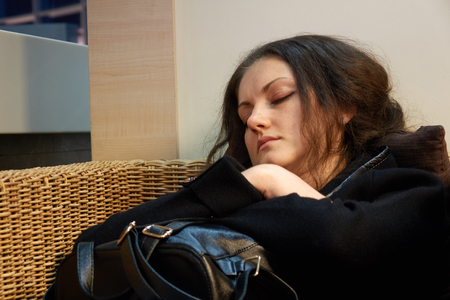 Girl is sleeping sitting in a wicker wood chair while waiting for departure.の写真素材