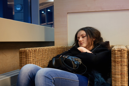 Girl is sleeping sitting in a wicker wood chair while waiting for departure.の写真素材