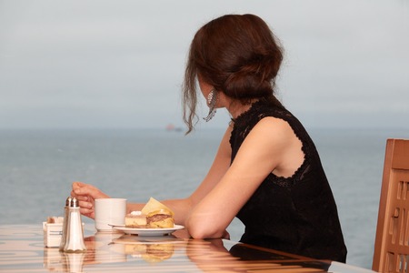 A girl in a cruise liner restaurant is eating a cake and looking out into the ocean closeup.の写真素材