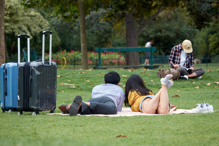 Asian loving couple of tourists with suitcases lies on the green grass in the park. The Champ de Mars in Paris.の写真素材