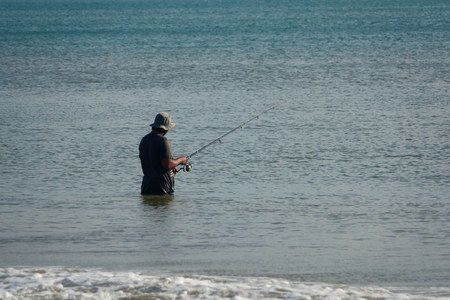 The fisherman catches fish in the sea on a fishing pole standing in water.の写真素材