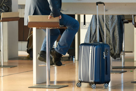 A business travel. A man with a modern suitcase sits on a bar stool in an airport.の写真素材