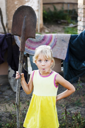 Girl making a face with a shovel in the yard of the rural houseの写真素材