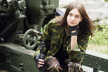 Girl in uniform with a submachine gun sitting on an artillery gun carriageの写真素材