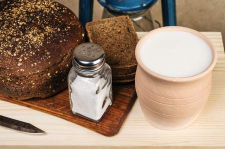 Milk in a clay pot, bread, salt on a cutting board. Still-life in the rustic styleの写真素材