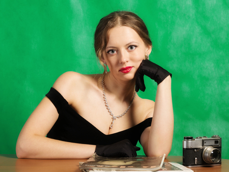 Girl in evening dress sitting at table with magazines. Studio portrait in retro styleの写真素材