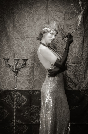 Girl in an evening dress with a cigarette mouthpiece. Studio portrait in retro style, toned in sepiaの写真素材