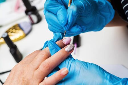 Manicurist applies a layer of gel polish to the clientâs nail. Brush pink nail polish. Covering the nail plate with nail polishの写真素材