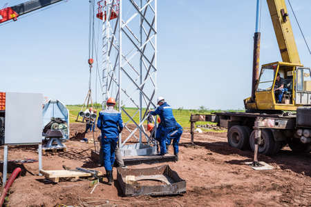 Workers at a construction site are using construction equipment to install a wind turbine tower....