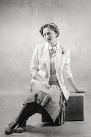 Young woman dressed in retro style sitting on a suitcase. Studio shotの写真素材