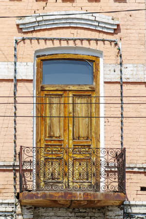 A wrought iron balcony with a wooden door on the facade of an old building. The picture was taken in Russia, in the city of Orenburgの写真素材