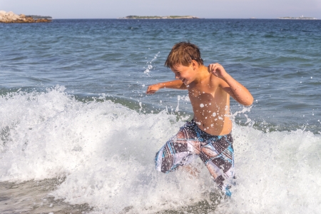 Happy boy running through the water at the beach