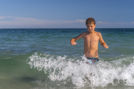 Happy boy running through the waves at the beachの写真素材