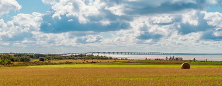 Panorama of hay bales on a farm along the ocean with the Confederation Bridge in the background (Prince Edward Island, Canada)の写真素材