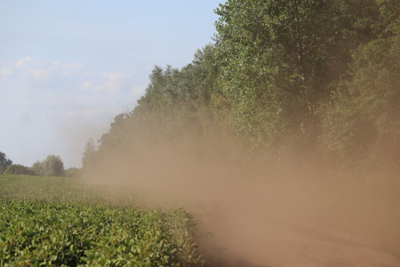 Dust along a dirt road near a field in summer.の写真素材