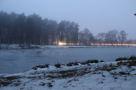 On the shore of a frozen lake in winter in the evening.の写真素材
