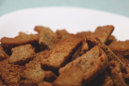 A close-up shot of a pile of golden brown, crispy bread rusks on a white plate with a blurred...