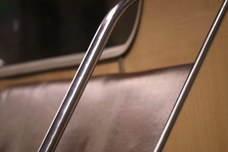 A close-up view of a shiny, metallic handrail inside an empty metro carriage, featuring reflections...