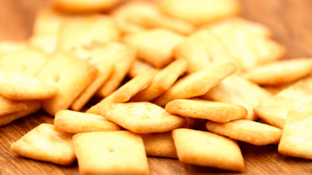 A close-up shot captures a heap of golden-brown square crackers, showcasing their crunchy texture...