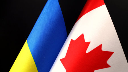 The flags of Ukraine and Canada are displayed closely together against a dark background,...