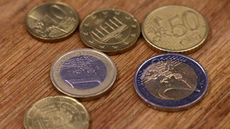 Several euro coins, including 1 and 2 euro pieces and various cents, are scattered across a warm,...